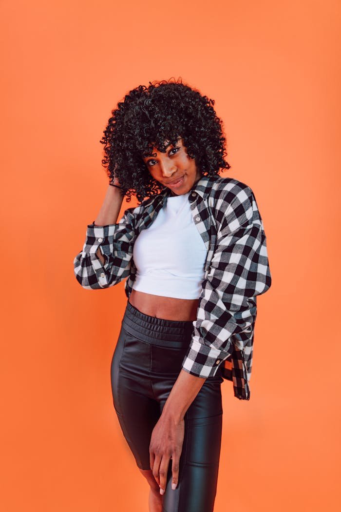 Young woman with curly hair in a trendy outfit against an orange background.